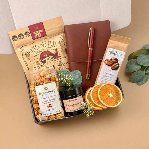 A gift box with a leather journal, pen, candle, coffee, popcorn and jerky